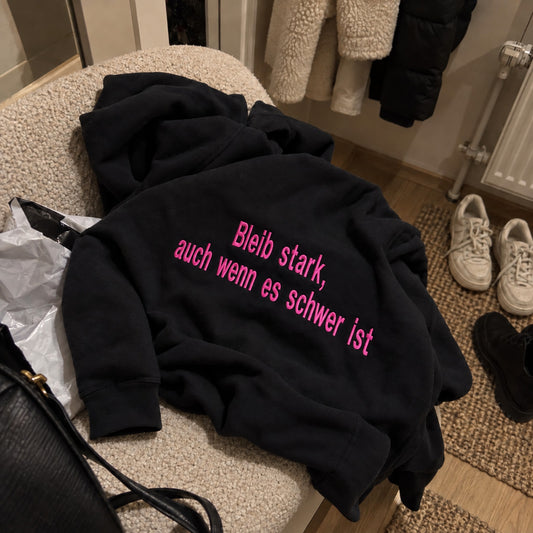 [DE] Schwarzer Hoodie mit pinker Stickerei: Bleib stark, auch wenn es schwer ist