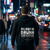 Man on a neon-lit street at night in a black zip hoodie with a motion-blur You Might Be Drunk print across the back