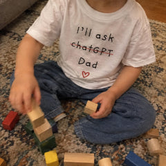 Child in a white I'll ask chatGPT Dad printed T-shirt playing with blocks