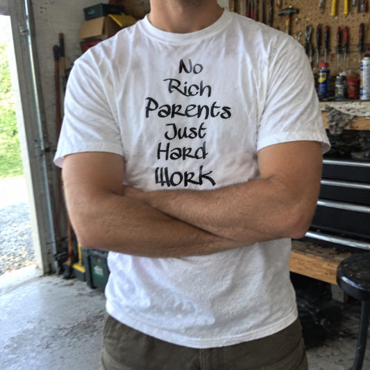 White No rich parents just hard work printed T-shirt worn in a workshop