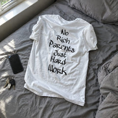 White No rich parents just hard work printed T-shirt lying on a bed