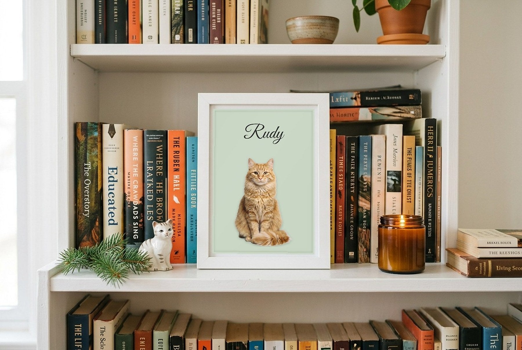 Mały plakat z rudym kotem i imieniem Rudy w białej ramce na półce z książkami