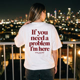 Woman at a rooftop bar at night in a white t-shirt with If You Need A Problem I'm Here printed across the back